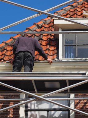 Worker on top of scaffolding repairing gutter on the roof