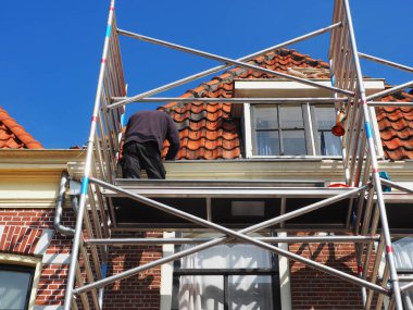Man in front of a house on top of scaffolding repairing the roof