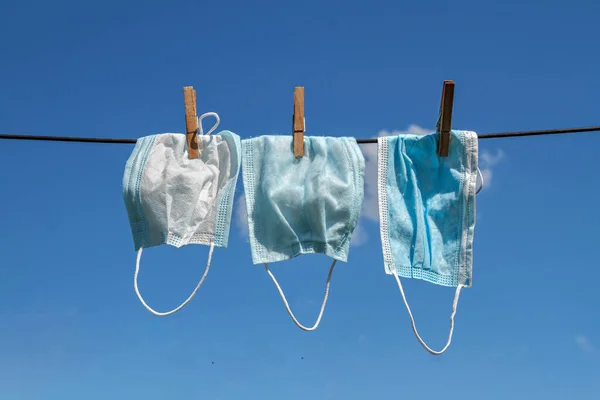 Three used washing face masks drying against a blue sky on a sunny day