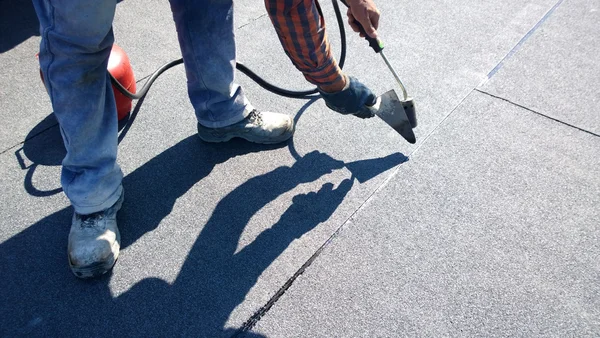 Roofer preparing part of bitumen roofing felt roll for melting by gas heater torch flame Royalty Free Stock Photos