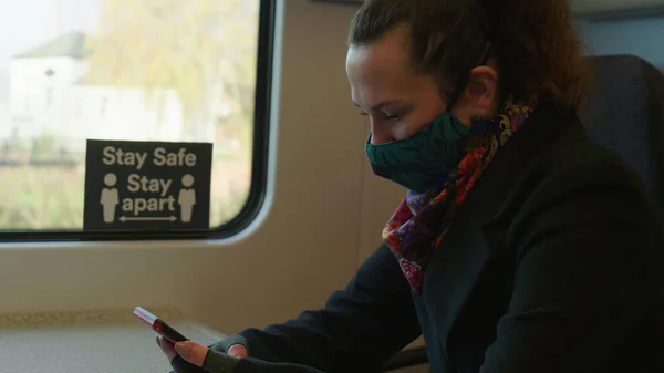 Kvinnlig passagerare bär ansikte täcka mask under covid-19 lockdown med hjälp av telefon inne tåg i england uk — Stockfoto