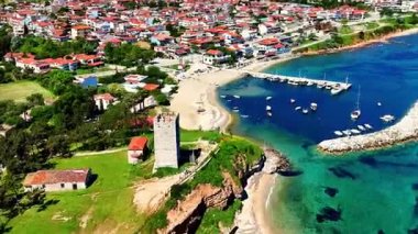 Drone view of Nea Fokaia in Chalkidiki, Greece, showing turquoise water, the harbour, fishing boats, and coastline under summer light.