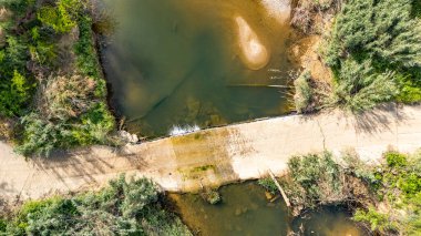 İlkbaharda Yunanistan 'ın Kalyves kenti yakınlarındaki zeytin bahçelerinden akan Vatonia Nehri' ni geçen bir yolun insansız hava aracı görüntüsü. Bu, Yunanlıların köprü kurmamasının tipik bir yaklaşımı..