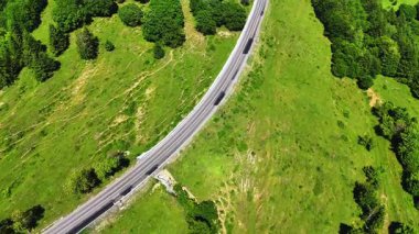 Romanya 'daki Oituz Geçidi' ni geçen, yeşil ormanlık tepeler ve parçalı bulutlu bir gökyüzü altında açık çayırlarla çevrili bir hava aracı videosu..
