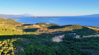 Yunanistan 'ın Ierissos kenti kıyılarından görülen Athos Dağı ve Ammouliani Adası' na doğru hava aracı görüntüsü, derin mavi deniz, uzak dağlar ve Ege Denizi üzerindeki berrak yaz ışığı.