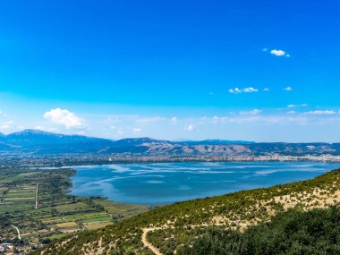 Wide panoramic view of Lake Pamvotida surrounded by mountains, wetlands, and farmland, with the city of Ioannina visible along the shoreline, Epirus region, Greece.