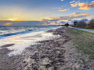 Yunanistan 'ın başkenti Chalkidiki' deki Nea Moudania yakınlarındaki Paralia Dionysou 'ya bakan Paralia Portaria sahilindeki akşam manzarası. Thermaic Körfezi 'nin dalgaları dramatik günbatımı bulutlarının altında çakıllı kıyılara yuvarlanıyor..