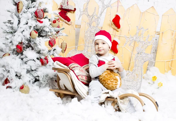 Petit garçon en costume de Noël assis sur un arbre de Noël — Photo