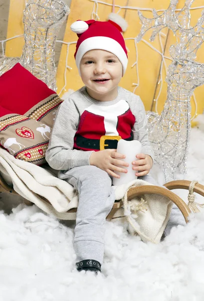 Niño en traje de Navidad sentado en un árbol de Navidad — Foto de Stock