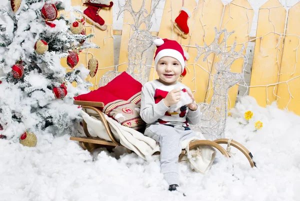 Niño en traje de Navidad sentado en un árbol de Navidad — Foto de Stock