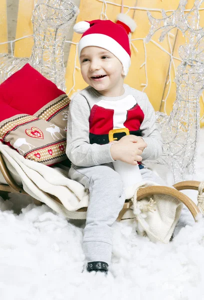 Niño en traje de Navidad sentado en un árbol de Navidad — Foto de Stock