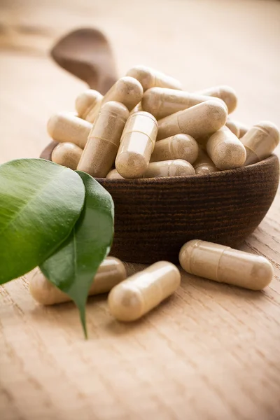 Medicina alternativa. Tabletas de medicina alternativa en una cuchara de madera, hoja verde . — Foto de Stock