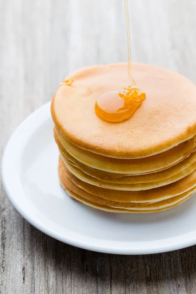 Stapel zelfgemaakte pannenkoeken met honing op houten achtergrond. — Stockfoto