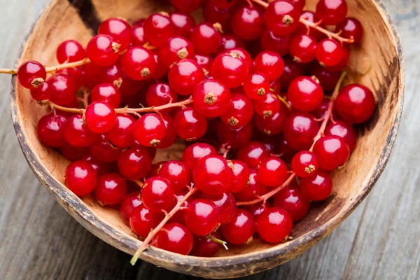Redcurrant on a branch close to a wooden bowl. — Stock Photo, Image