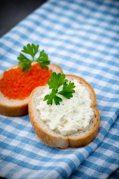 Pan con queso crema fresco y caviar rojo en la mesa . — Foto de Stock