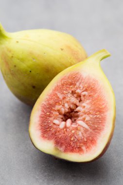 Gri bir masanın üzerinde tam bir incir ve bir incir dilimlenmiş.. 