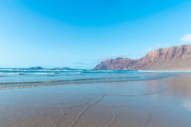 Güzel sahil manzarası ve tropikal Lanzarote denizi. Kanaryalar. Famara Sahili, Lanzarote Adası, Kanarya Adaları. Lanzarote adasındaki en popüler plajda turistler.