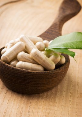 Alternatif ilaç tabletleri tahta kaşıkta, yeşil yapraklı..