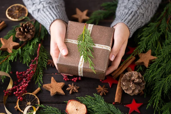 木のテーブルの上に置かれたクリスマスプレゼントを保持する女性 — ストック写真