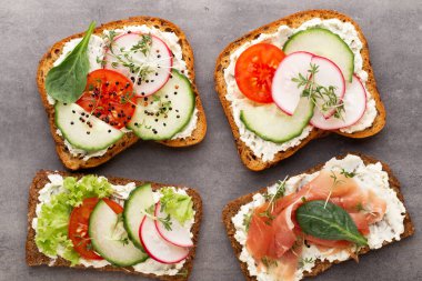 Krem peynirli, sebzeli ve salamlı mini sandviçler. Salatalıklı sandviçler, turp, domates, gri arka planda salam, üst manzara. Düz yatıyordu.