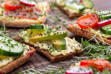 Krem peynirli, sebzeli ve salamlı mini sandviçler. Salatalıklı sandviçler, turp, domates, gri arka planda salam, üst manzara. Düz yatıyordu.