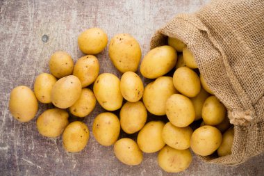 Ahşap arka planda taze çiğ patates çuvalı..