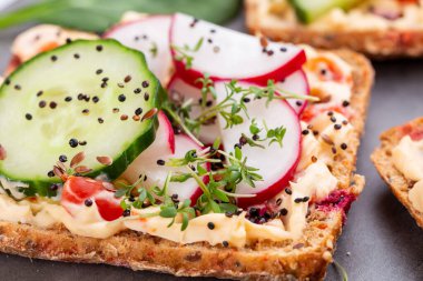 Krem peynirli, sebzeli ve salamlı sandviç. Salatalıklı sandviçler, turp, domates, gri arka planda salam, üst manzara. Düz yatıyordu.