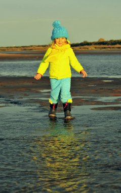 Küçük kız bir günbatımı kum sonbahar plajındaki. 