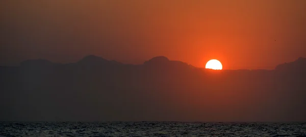 Pôr do sol no oceano com montanhas — Fotografia de Stock