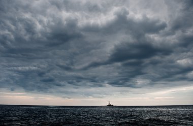Bulutlu gökyüzü ve deniz feneri ile dalgalı okyanus