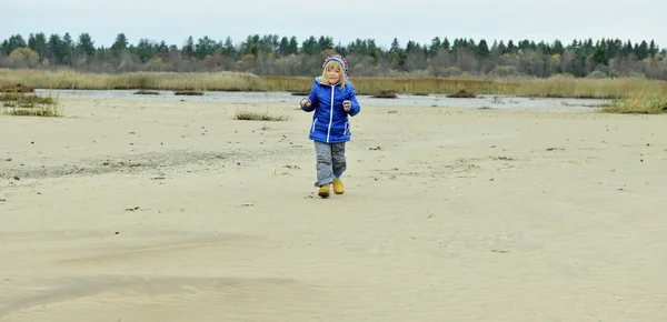 La bambina va sulla costa sabbiosa in abiti invernali . — Foto Stock