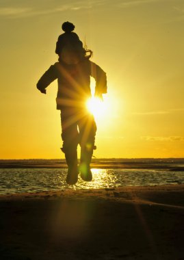 Little girl jumping on the ocean shore in backlight sunset.