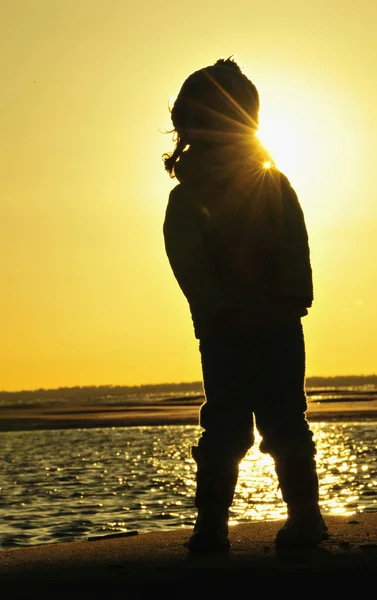 Bambina che salta sulla riva dell'oceano in controluce al tramonto . — Foto Stock