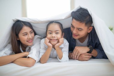 Mutlu sevgi dolu bir aile, baba anne ve çocuk yatakta oynuyor.