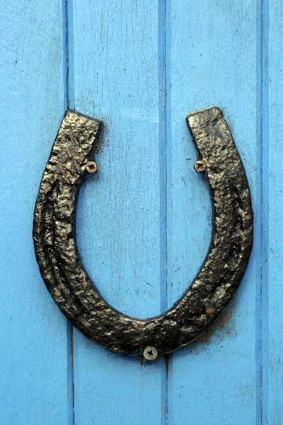 Svart hästsko, fastspikad på blå dörren — Stockfoto