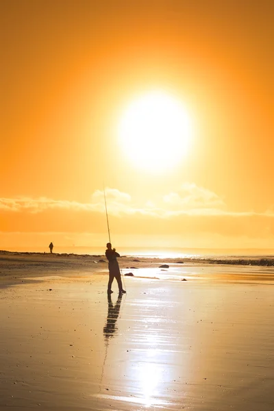 Pescador solitario que pesca en la playa del atardecer —  Fotos de Stock