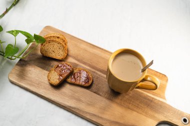 Reçelli hafif tost ve beyaz arka planda tahta bir tahtada sütlü büyük turuncu bir fincan kahve..