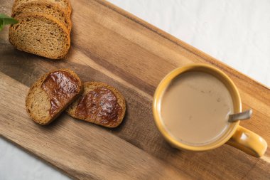 Reçelli hafif tost ve beyaz arka planda tahta bir tahtada sütlü büyük turuncu bir fincan kahve..
