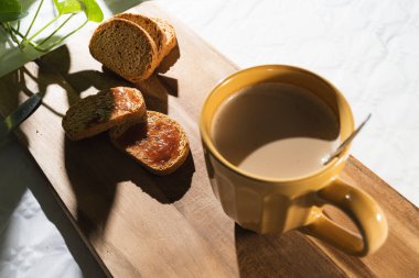 Reçelli hafif tost ve beyaz arka planda tahta bir tahtada sütlü büyük turuncu bir fincan kahve..