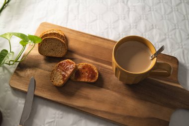 Reçelli hafif tost ve beyaz arka planda tahta bir tahtada sütlü büyük turuncu bir fincan kahve..