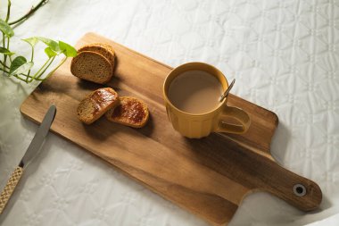 Reçelli hafif tost ve beyaz arka planda tahta bir tahtada sütlü büyük turuncu bir fincan kahve..