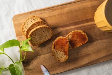 Reçelli hafif tost ve beyaz arka planda tahta bir tahtada sütlü büyük turuncu bir fincan kahve..