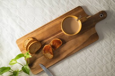 Reçelli hafif tost ve beyaz arka planda tahta bir tahtada sütlü büyük turuncu bir fincan kahve..