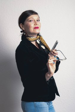 Siyah ceketli ve gözlüklü bir kadın cep telefonu tutuyor. Sarı bir eşarp takıyor ve mavi ojeli.