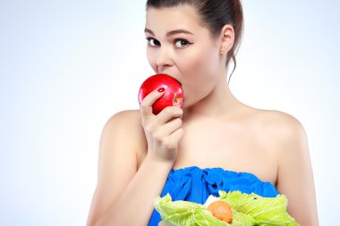 Funny girl eating vegetables on light background clipart