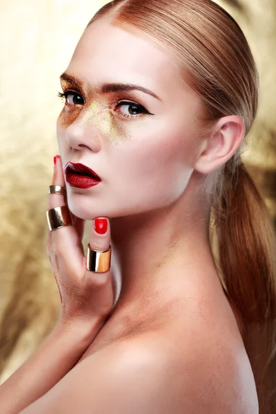 Närbild porträtt av sexig ung kvinna med vackra blå ögon och röda läppar på guld bakgrund — Stockfoto
