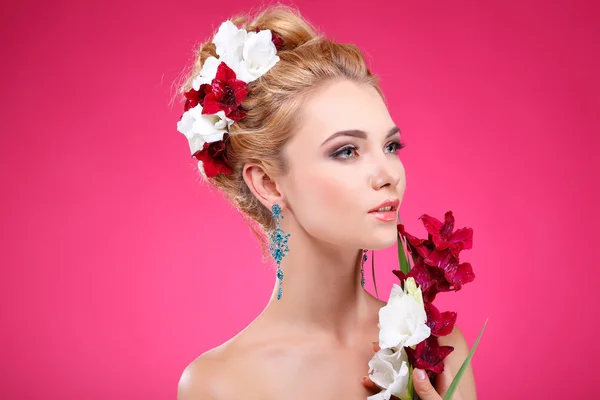 Mooi meisje, geïsoleerd op een roze achtergrond met gekleurde bloemen in haren, emoties, cosmetica — Stockfoto