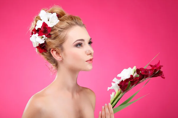 Bella ragazza, isolata su uno sfondo rosa con fiori varicolore nei capelli, emozioni, cosmetici — Foto Stock