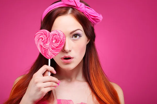 Retrato de hermosa chica pelirroja alegre con un gran caramelo sobre un fondo rosa Imagen de archivo