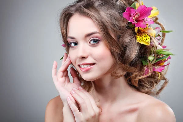 Vacker flicka, isolerad på en ljus - grå bakgrund med varicoloured blommor i hårstrån, känslor, kosmetika — Stockfoto
